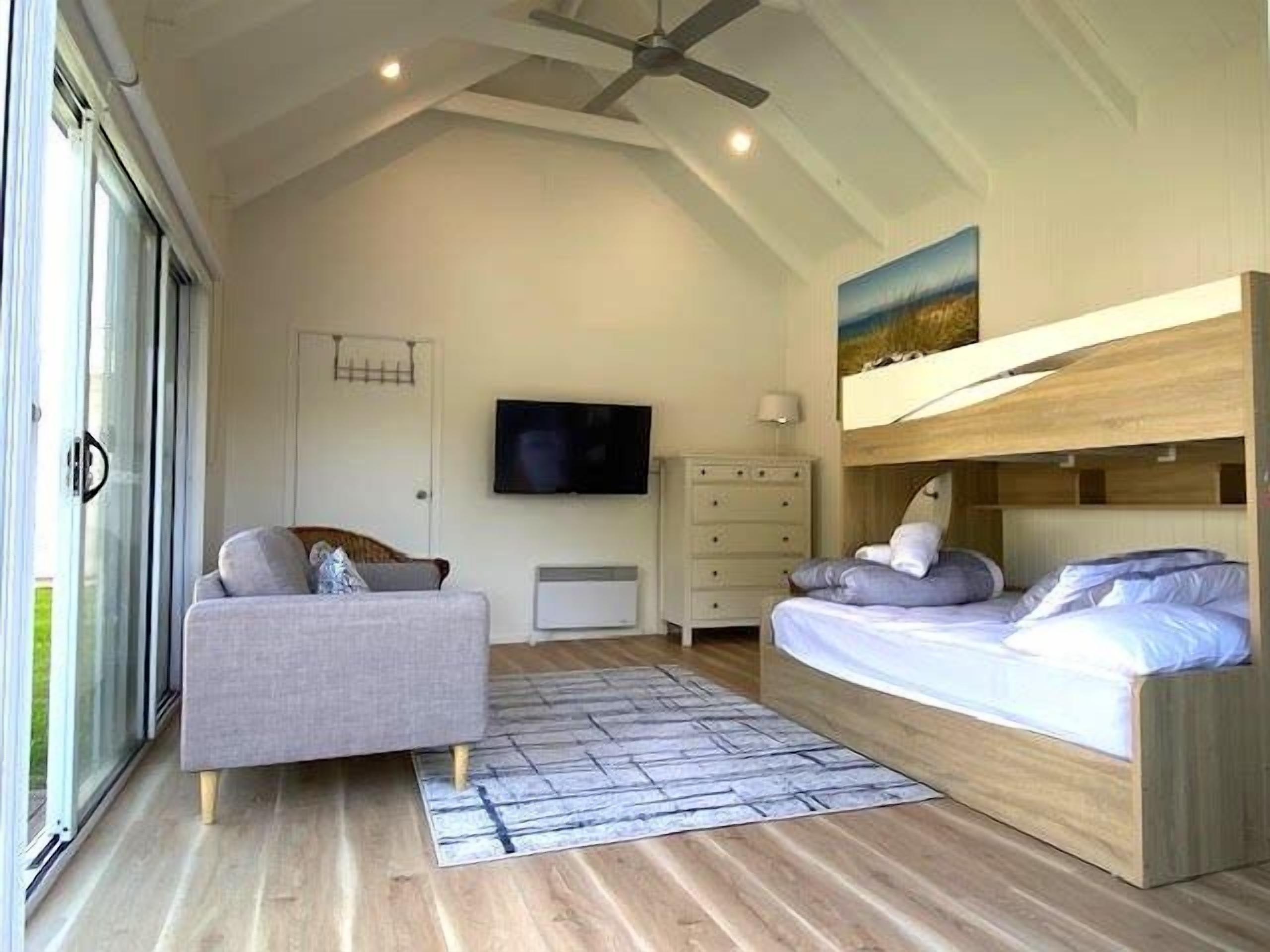 A bedroom with a bunk bed, a sofa, a flat-screen TV, and a sliding glass door.