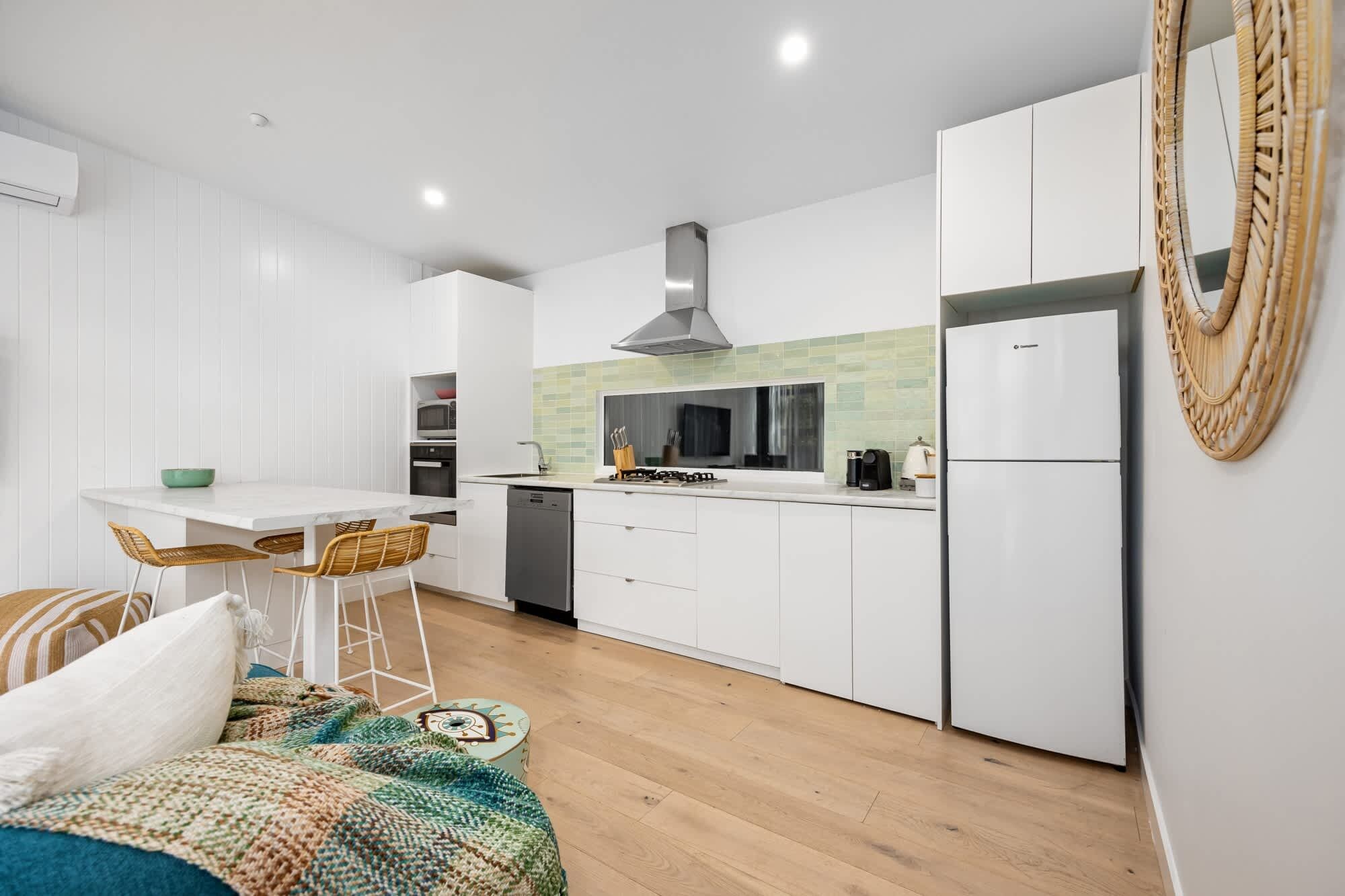 A modern kitchen with white cabinetry, a dining area with a white table and wicker chairs, and a large woven basket on the wall.