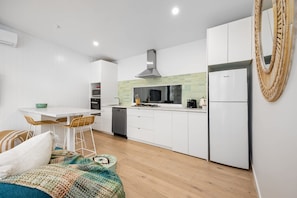 Una cucina moderna con mobili bianchi, un'area pranzo con tavolo bianco e sedie in vimini, e un grande cesto di vimini a parete.