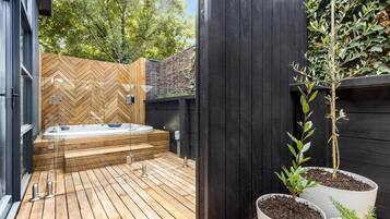 A wooden deck with a hot tub, potted plants, and a black fence.