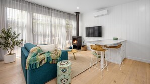 A modern living room with a sofa, a small table, a TV, and a fireplace. - The Love Shack, Blairgowrie - Romantic, private bungalow, walk to Blairgowrie village and beach (BLAIRGOWRIE)