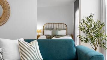 A modern bedroom with a bed, a blue sofa, and a potted plant.