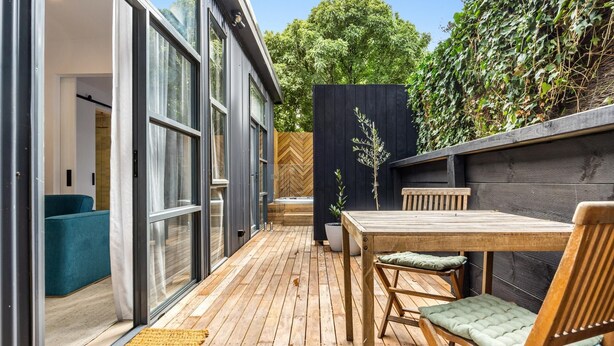 A modern patio with a wooden deck, a table with chairs, and a view of a lush garden. - The Love Shack, Blairgowrie - Romantic, private bungalow, walk to Blairgowrie village and beach (BLAIRGOWRIE)