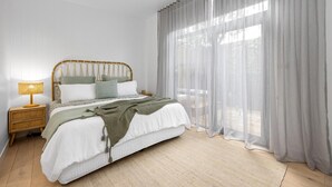 A bedroom with a bed, a bedside table, a lamp, and sheer curtains. - The Love Shack, Blairgowrie - Romantic, private bungalow, walk to Blairgowrie village and beach (BLAIRGOWRIE)