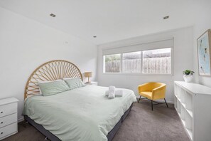 Une chambre à coucher comprenant un lit, une chaise, une table de chevet, une fenêtre et une étagère fixée au mur.