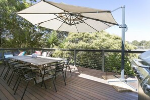An outdoor deck with a table and chairs, a grill, and a large umbrella providing shade.