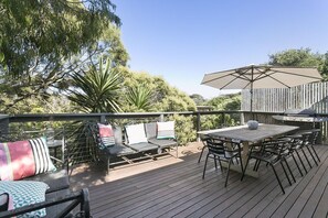 Une terrasse extérieure avec une plateforme en bois, une table et des chaises, un barbecue et un coin salon agrémenté de coussins.