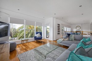 Un salon moderne avec une grande fenêtre, un fauteuil bleu, un canapé gris et une table basse en verre.
