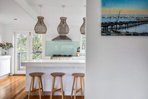 Une cuisine équipée d’une cuisinière à gaz, de luminaires suspendus en osier et offrant une vue sur le port de plaisance grâce à une porte vitrée.