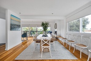 Un vaste espace dédié à la salle à manger, avec une table en bois et des chaises blanches, une grande fenêtre offrant une belle vue et un tableau accroché au mur.