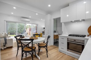 A modern kitchen with white cabinets, a built-in oven, and a dining area with a round table and chairs.