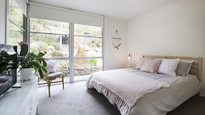 A bedroom with a bed, a chair, a desk with a plant, and a window with a view of the outside.