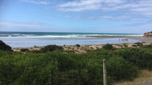A beach with a clear sky, waves, and a fence in the foreground.