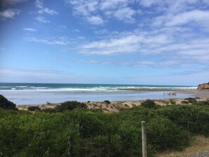 A beach with a clear sky, waves, and a fence in the foreground.
