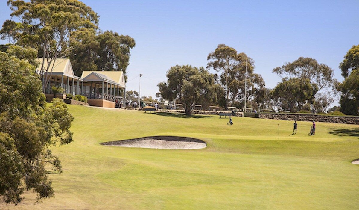 A golf course with a building, trees, and a clear sky.
