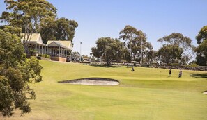 A golf course with a building, trees, and a clear sky.
