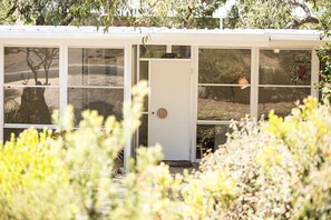 Una pequeña construcción cerrada con varias ventanas y una puerta, rodeada de vegetación.