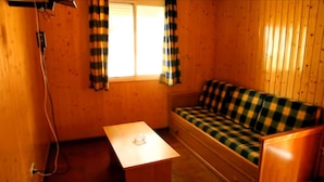 A small cabin with a wooden interior, a checkered sofa, a small table, and a window with curtains.