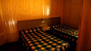 A room with two single beds, wooden walls, and a small table.