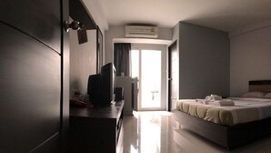 A hotel room with a bed, a desk, a television, and an air conditioning unit. - Grand Seven Place (Pak Kret)