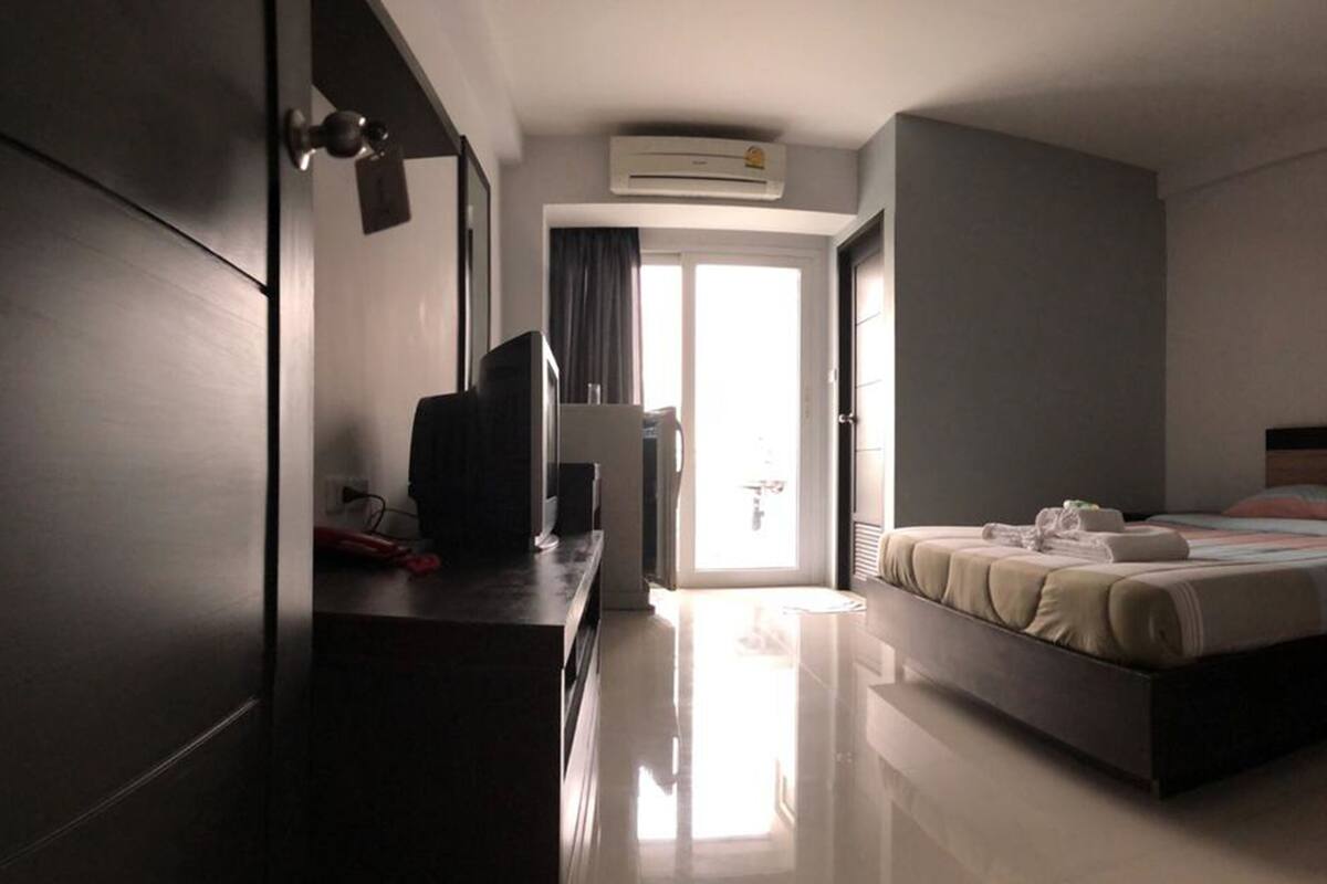 A hotel room with a bed, a desk, a television, and an air conditioning unit.