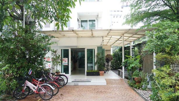 A covered outdoor area with a paved walkway, a row of bicycles, and a building entrance with glass doors. - Grand Seven Place (Pak Kret)