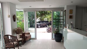 A modern interior with a seating area, a large potted plant, and a view of the outside. - Grand Seven Place (Pak Kret)