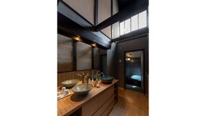 Une salle de bain moderne avec un meuble-lavabo en bois, deux grands lavabos et une baignoire visible à travers une porte.