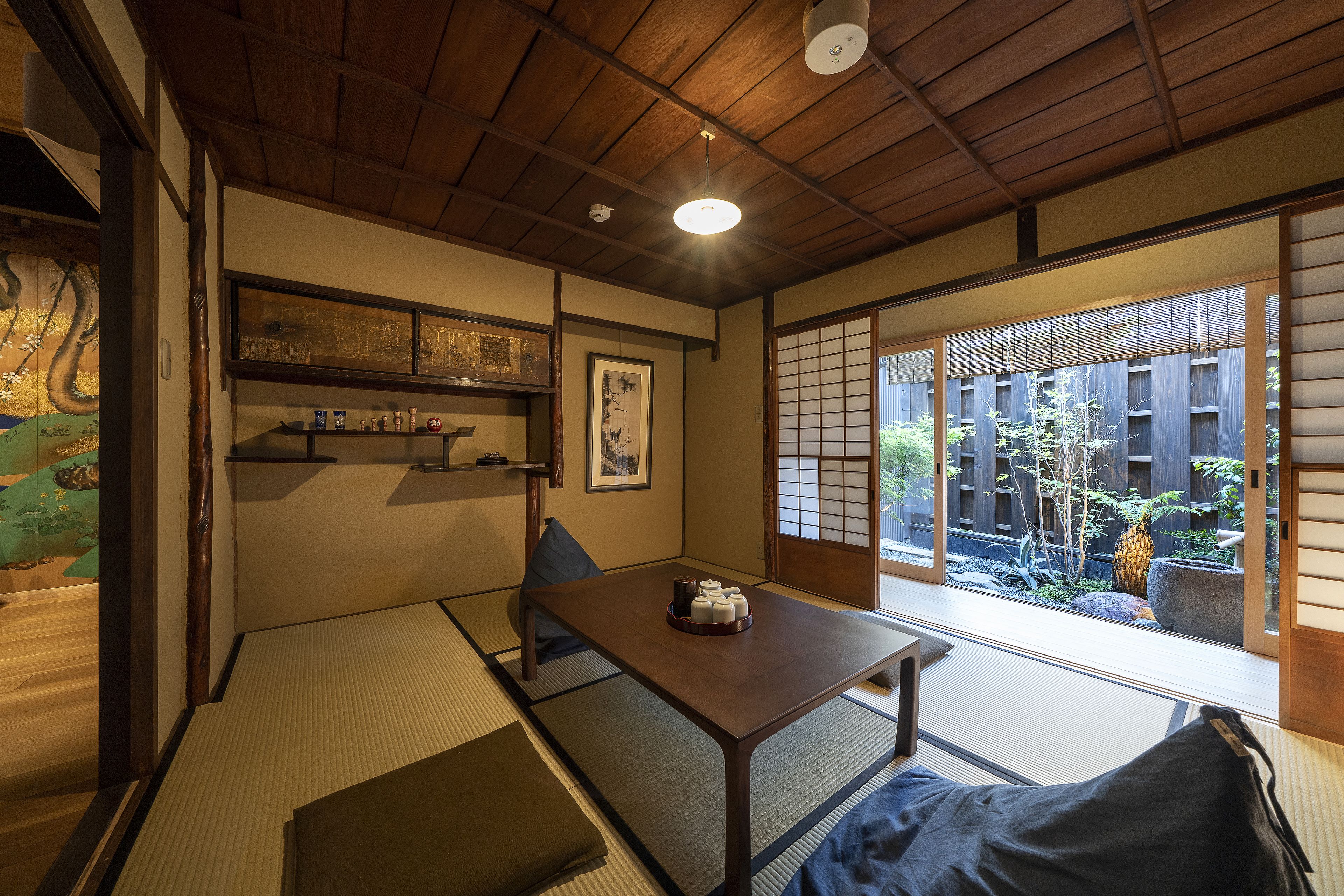 A traditional Japanese room with tatami flooring, a low wooden table, and sliding doors leading to a garden.