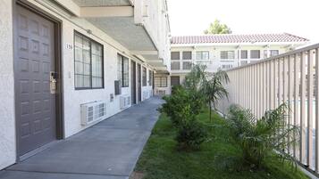 Una hilera de edificios de estilo residencial con números en las puertas, un sendero de concreto y una pequeña zona verde con plantas.