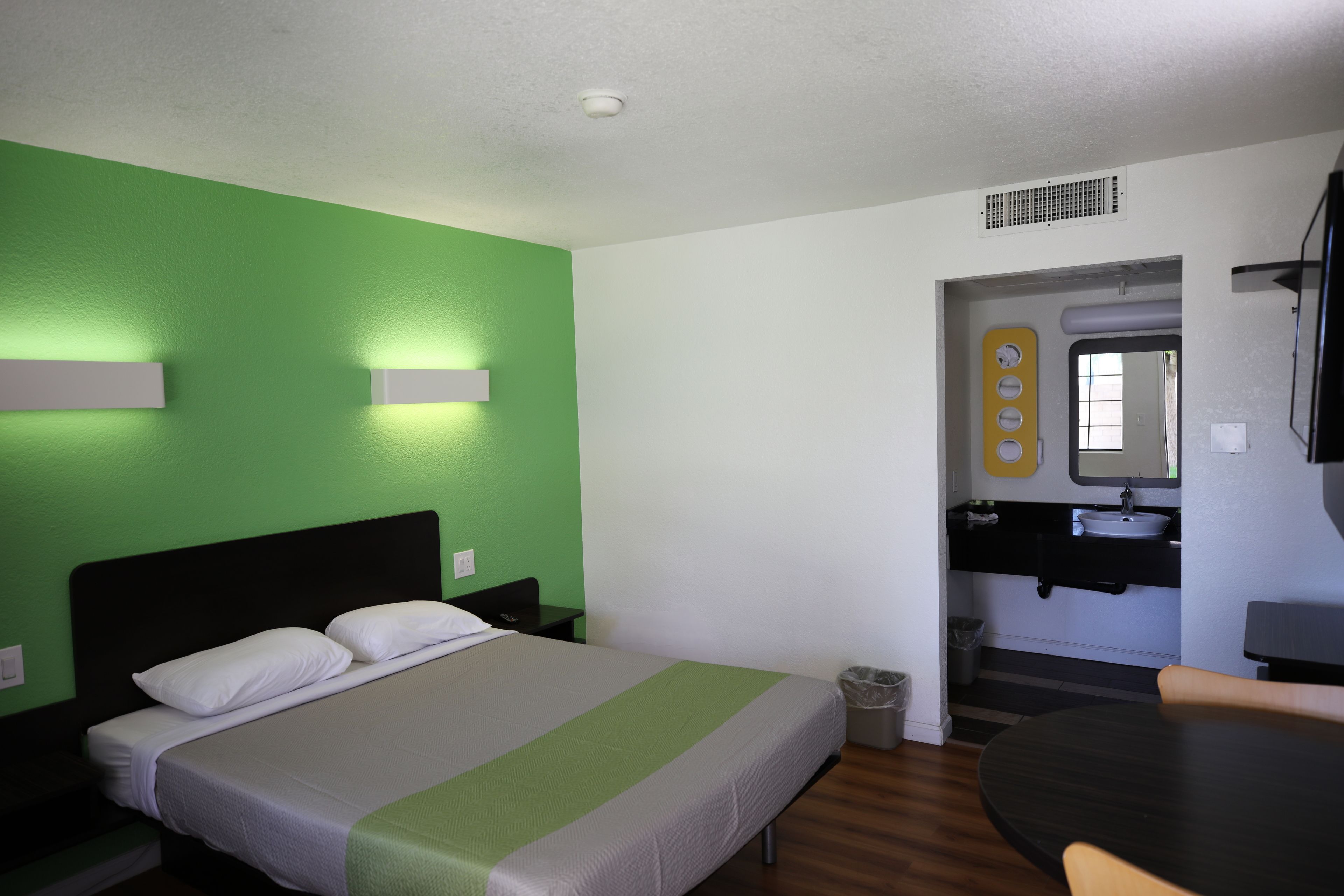 A hotel room with a bed, a small table, a chair, a bathroom with a sink and mirror, and a television.