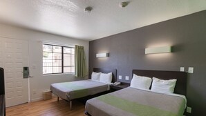 A hotel room with two beds, a window with curtains, a door, and a wall-mounted light fixture. - Studio 6 Barstow, CA (Barstow)