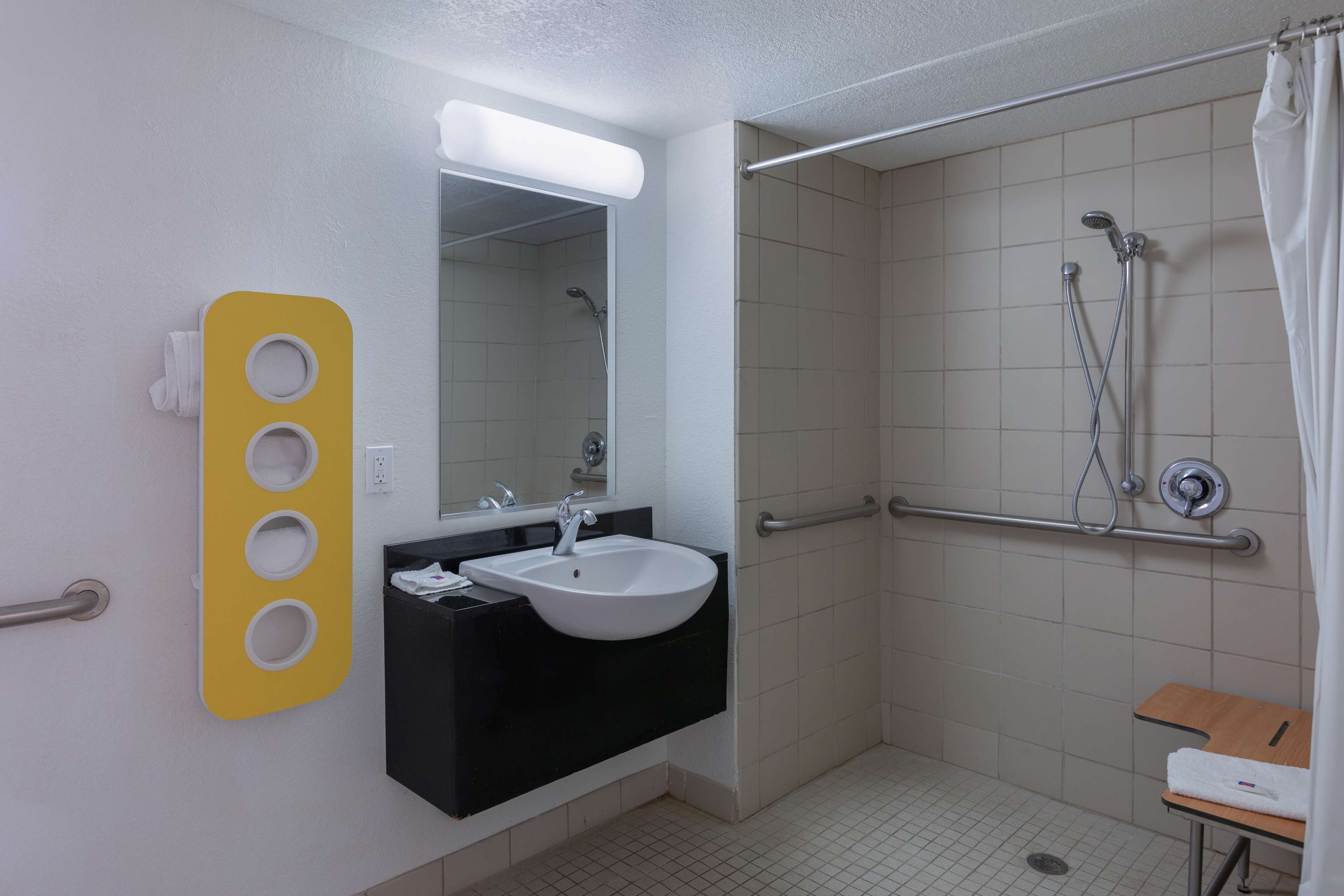 Une salle de bain avec un lavabo blanc, un plan de toilette noir et un distributeur de savon jaune.