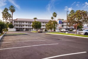 A multi-story motel with a parking lot, palm trees, and a clear blue sky. - Studio 6 Fairfield, CA - Napa Valley (Fairfield)
