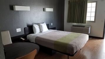 A hotel room with a bed, bedside table, chair, and a window with curtains.