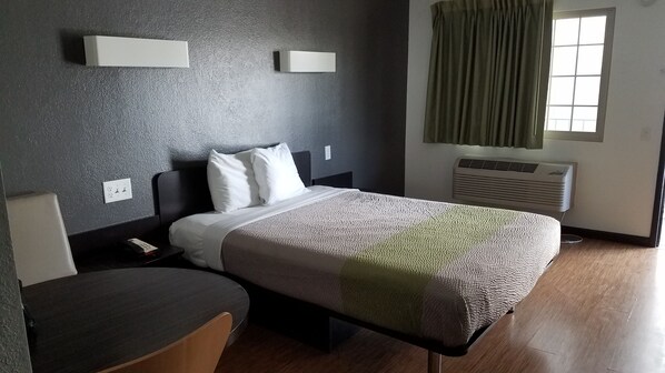 A hotel room with a bed, bedside table, chair, and a window with curtains.