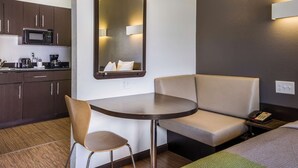 Ett kompakt hotellrum med ett litet pentry, ett runt bord, en soffa och en spegel.
