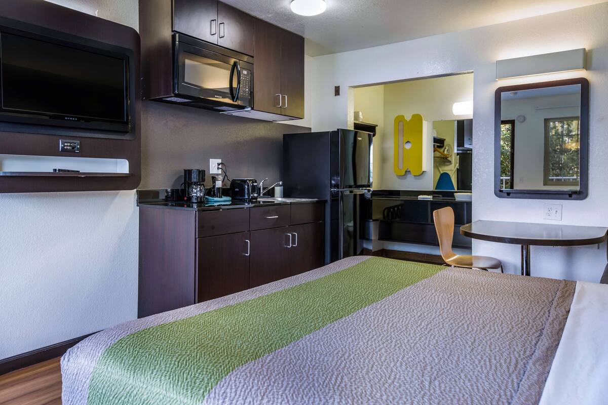 Une chambre d’hôtel équipée d’un lit, d’une kitchenette, d’une télévision, d’un four à micro-ondes et d’un miroir.