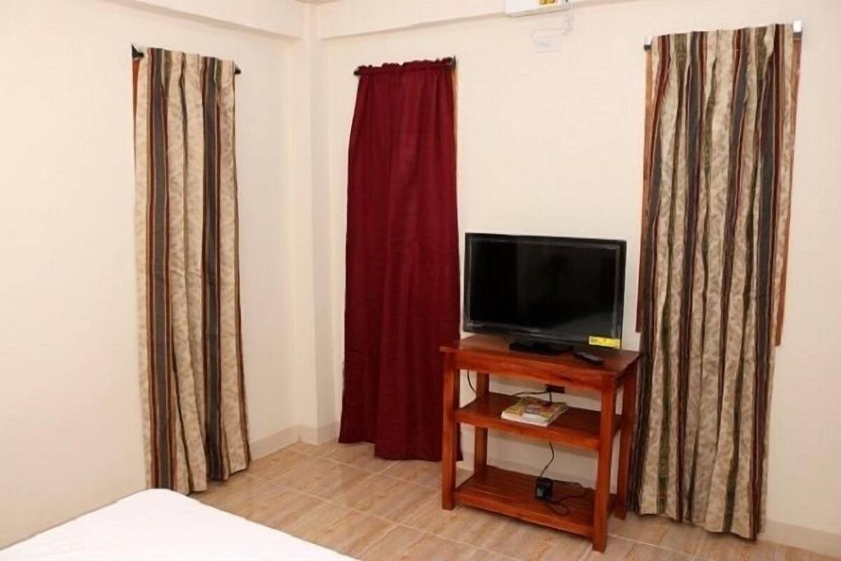 Une chambre avec un lit, un téléviseur posé sur un meuble en bois et des rideaux.