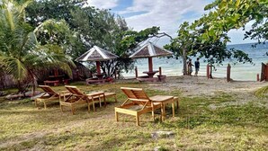 A beachside area with wooden lounge chairs, thatched-roof structures, and a view of the sea. - D's Ocean View Beach Resort (Siquijor)