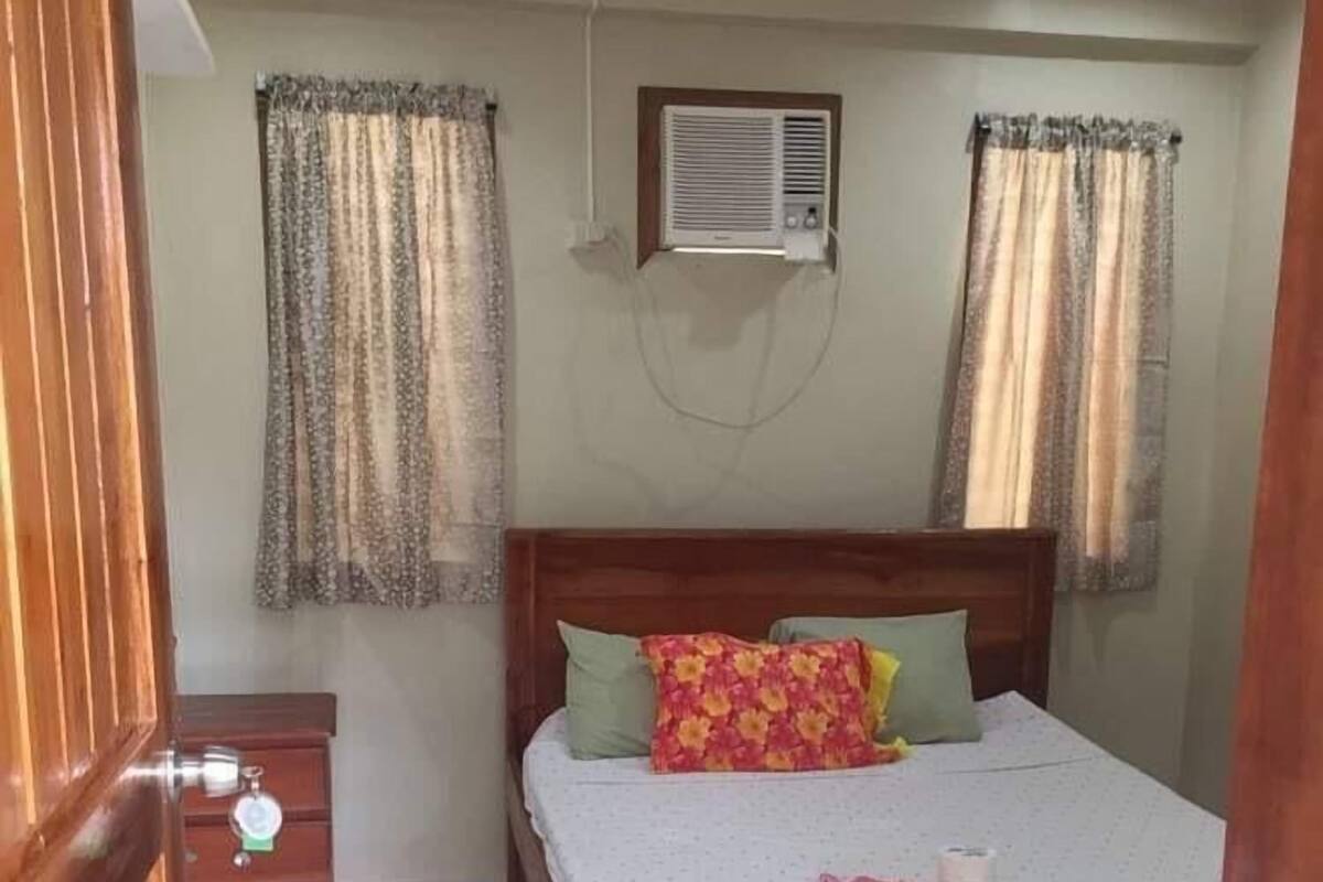 Une chambre avec un lit en bois, une table de chevet, un appareil de climatisation et des rideaux.