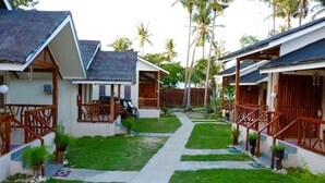 A row of bungalow-style accommodations with wooden railings and thatched roofs, surrounded by a well-maintained lawn and palm trees. - D's Ocean View Beach Resort (Siquijor)