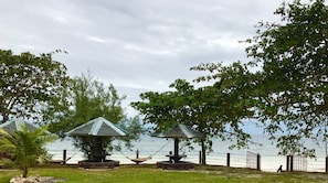 A seaside view with three thatched-roof gazebos, a hammock, and a fence overlooking the water.