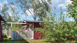 Ein kleines, rotes Blockhaus mit Veranda, umgeben von einem Holzzaun und üppiger Vegetation.