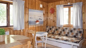 Ein gemütliches Blockhäuschen im Inneren, mit Holzvertäfelung, einer Couch mit Patchwork-Überzug, einem Esstisch mit Stühlen und einer Wanduhr.