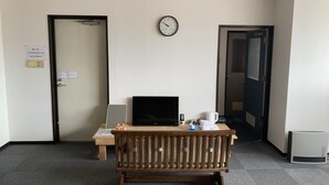 A hotel room with a wooden desk, a flat-screen TV, a clock on the wall, and a door with a sign indicating Wi-Fi availability. - Yamanami'Tel - Hostel (Kumamoto)