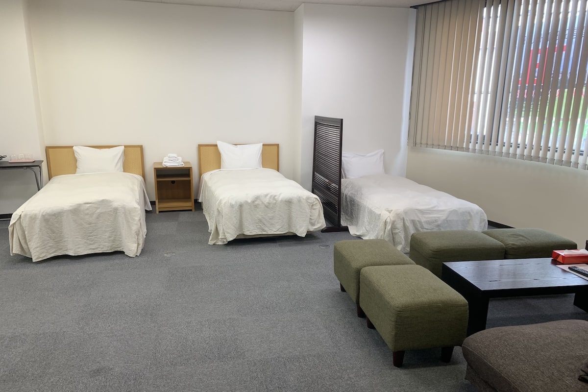 Ein Hotelzimmer mit zwei Einzelbetten, einem Schlafsofa, einem Tisch und einem Heizlüfter.