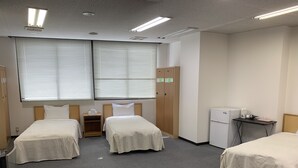 A hotel room with two single beds, a small desk with a refrigerator, and a wardrobe. - Yamanami'Tel - Hostel (Kumamoto)