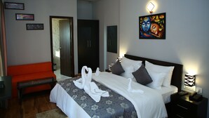 A hotel room with a bed, a nightstand, a bedside table, a chair, and a painting on the wall. - Anandam Clarks Inn Suites Vrindavan (Mathura)
