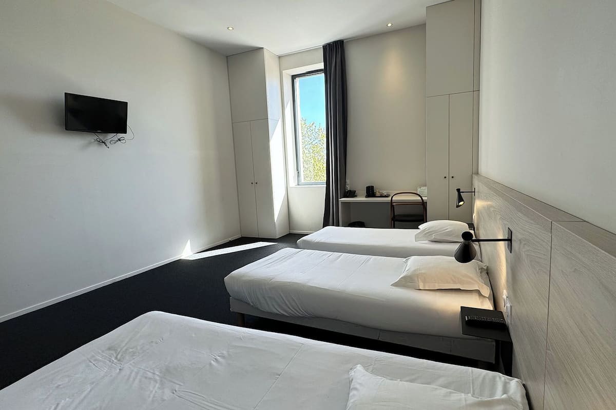 Habitación de hotel con dos camas, televisión, escritorio y ventana con cortinas.